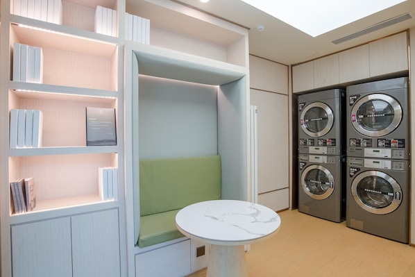 A laundry room with two stacked washing machines and a seating area with a table. - Ji Hotel (Beijing)