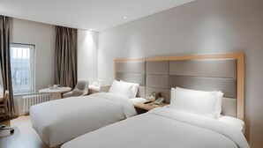 A hotel room with two beds, a small table, a chair, a window with curtains, and a radiator. - Ji Hotel (Beijing)
