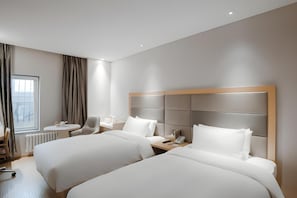 A hotel room with two beds, a small table, a chair, a window with curtains, and a radiator. - Ji Hotel (Beijing)