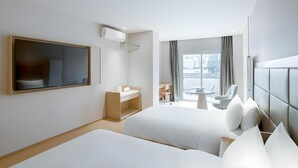 A modern hotel room with two beds, a large mirror, a bedside table, a built-in TV, a window with curtains, and a view of the outside.