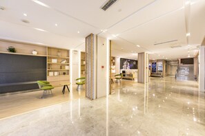 Un hall d’hôtel moderne avec un sol en marbre, des étagères en bois et des chaises vertes.