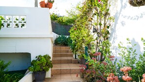 Un escalier menant à un bâtiment blanc, agrémenté de plantes en pot et de plantes grimpantes en fleurs.