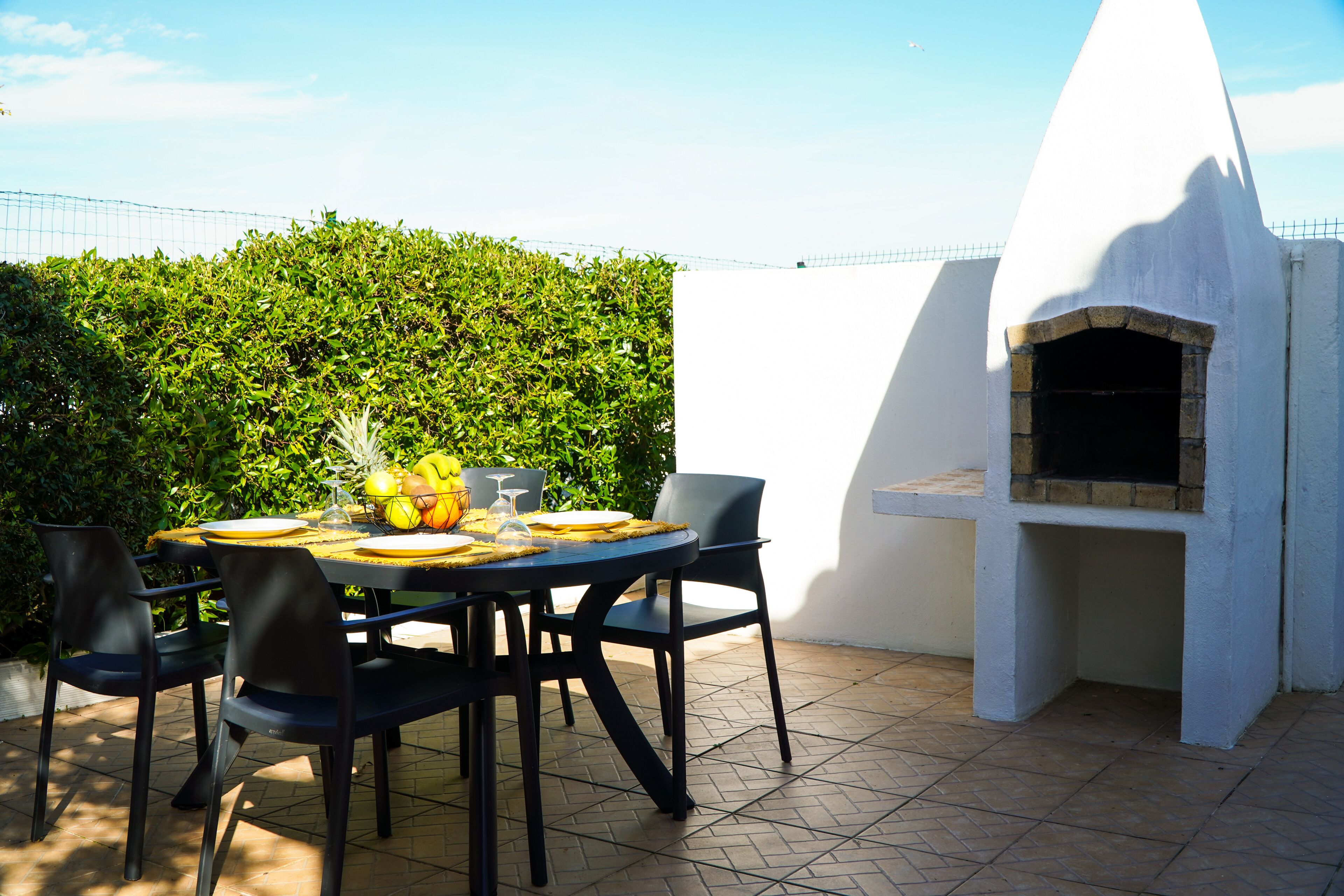Zona pranzo all'aperto con tavolo rotondo, sedie e forno a legna.