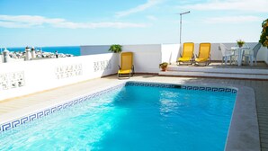 Une piscine bordée de carreaux aux motifs géométriques, entourée d’un mur blanc et offrant une vue sur la mer.