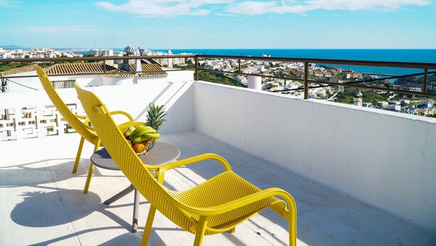 Un balcon avec des chaises jaunes et une petite table, donnant sur un paysage urbain le long de la côte.