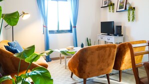 Un salon avec un canapé, une table, des chaises, un téléviseur et une fenêtre avec des rideaux.
