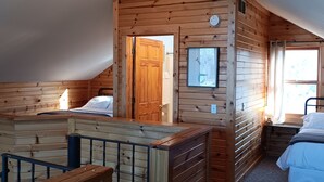 A wooden cabin with a loft bedroom, a small bathroom, and a balcony.