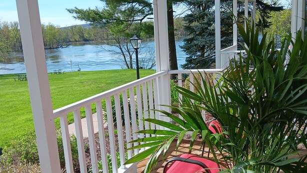 A wooden deck with a white railing, a potted plant, and a red chair.
