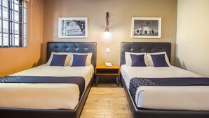 Una camera d'albergo con due letti, pavimento in legno e due quadri appesi alle pareti.
