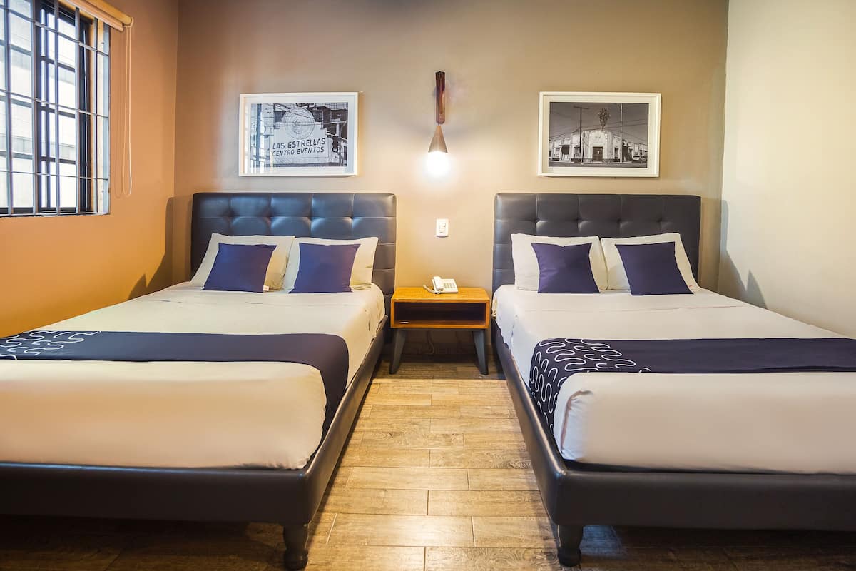 Habitación de hotel con dos camas, piso de madera y dos cuadros en las paredes.