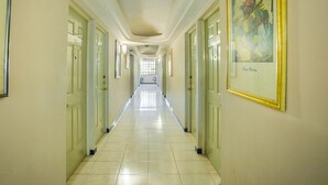 Un corridoio con porte su entrambi i lati, pavimento piastrellato e un quadro appeso alla parete destra.
