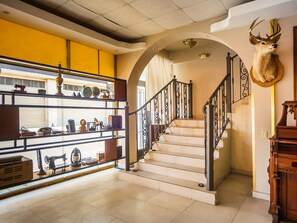 Un escalier avec une rampe en fer forgé, une tête de cerf fixée au mur et une étagère sur laquelle sont disposés divers objets.
