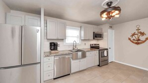 A modern kitchen with stainless steel appliances, white cabinetry, a microwave, a coffee maker, and a decorative wall anchor.