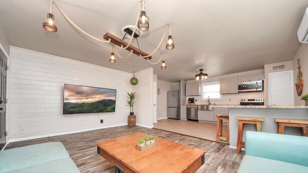 A spacious living area with a wooden dining table, light blue sofas, and a large flat-screen TV mounted on the wall.