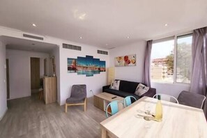 A modern living room with a wooden dining table, a sofa, and a coffee table. There are two chairs, a painting on the wall, and a window with curtains. - Penthouse − Marbella Centre, Pool + Close to Beach (Marbella)