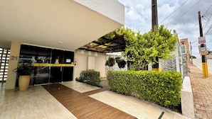 A modern building with a covered entrance, a tiled pathway, and greenery.