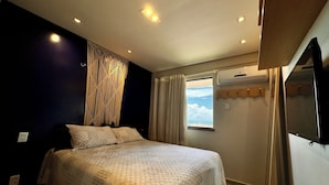 A bedroom with a bed, a macrame wall hanging, an air conditioning unit, a window with curtains, and a view of the sky.