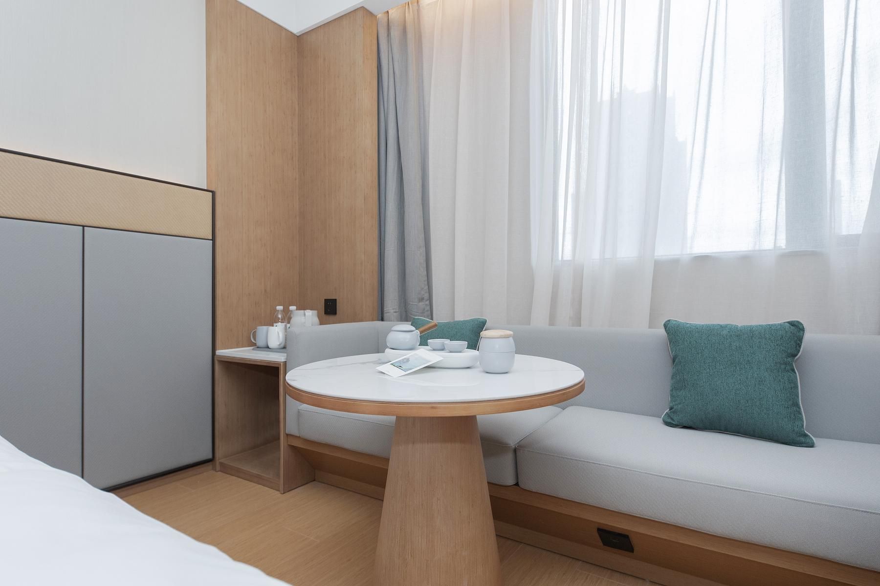 Una habitación de hotel moderna con sofá, una mesa redonda y una mesita auxiliar con una tetera y tazas.