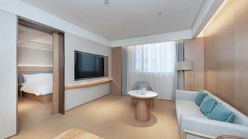 Una habitación de hotel moderna con cama, televisión, sofá, una mesita y ventana con cortinas.