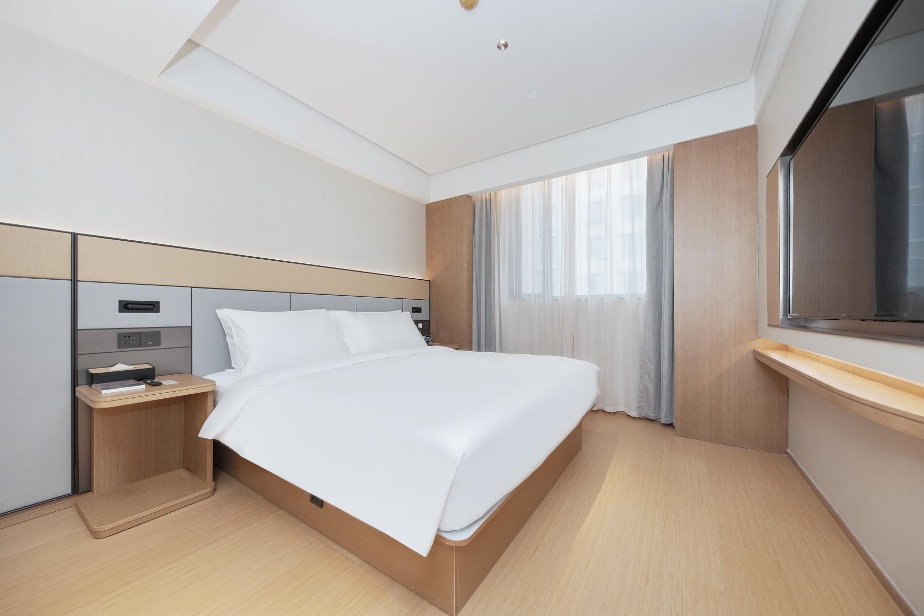 A modern hotel room with a large bed, a desk, and a large window.