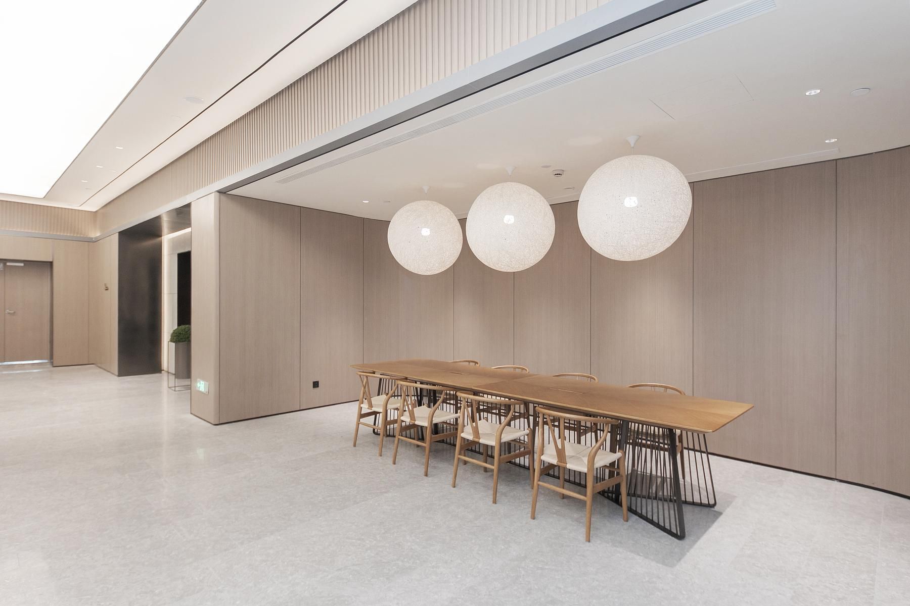 A modern conference room with a long wooden table and chairs, large spherical pendant lights, and a minimalist design.