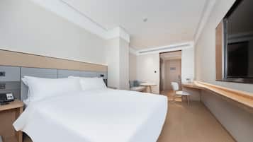 Quarto de hotel com cama grande, escrivaninha, cadeira, televisão e porta que dá para outro cômodo.