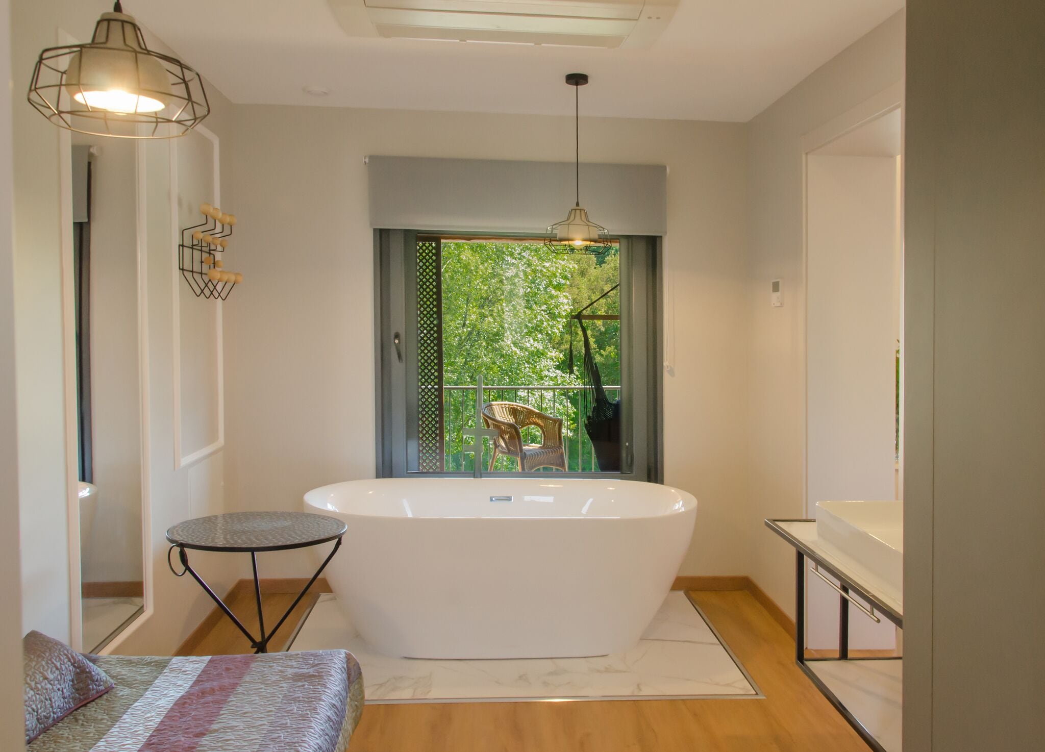 A modern bathroom with a freestanding bathtub, a small round table, and a hanging chair by the window.