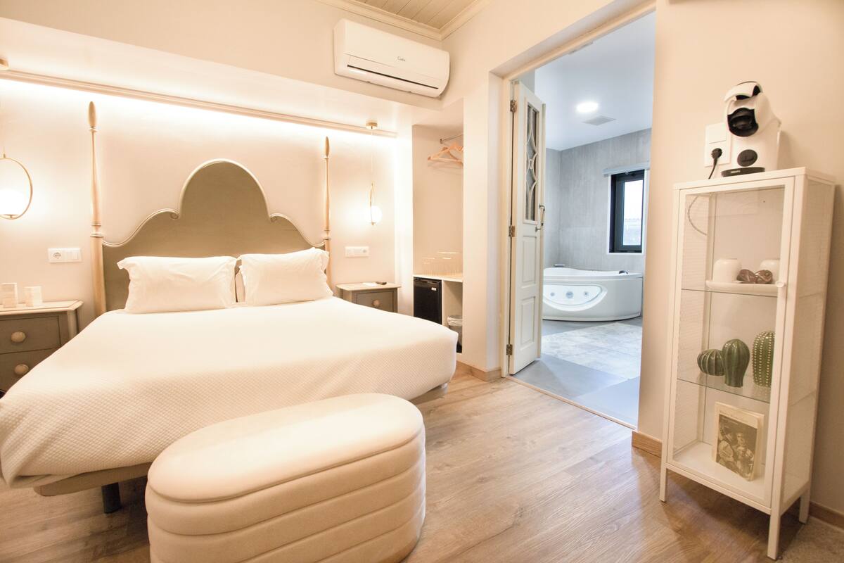 A modern bedroom with a large bed, bedside tables, a wardrobe, and an air conditioning unit.