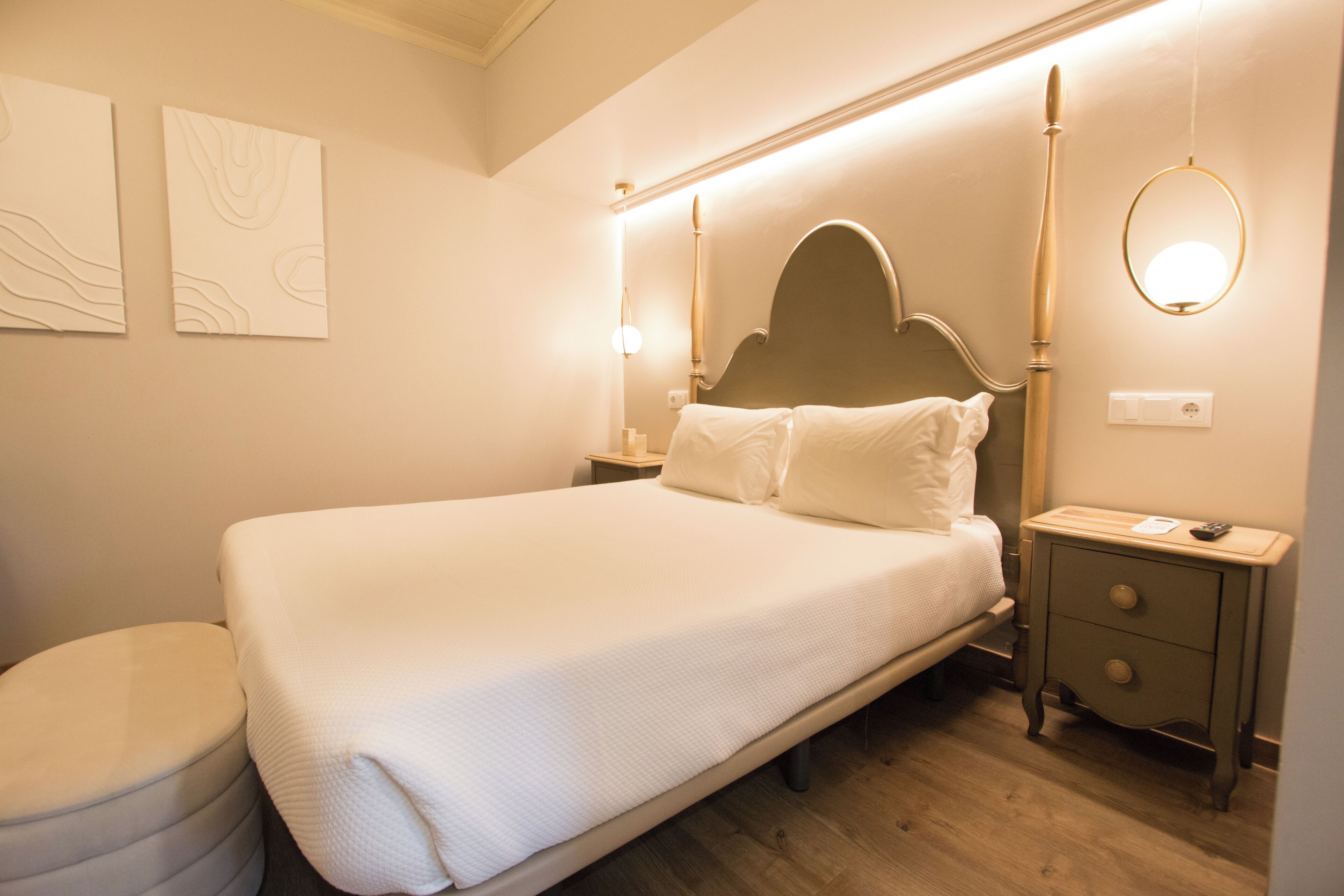A neatly made bed with a wooden headboard, a bedside table with a lamp, and a small drawer unit.