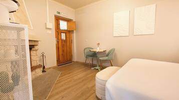 A hotel room with a wooden floor, a bed, a small round table with two chairs, and a door with a sign above it.