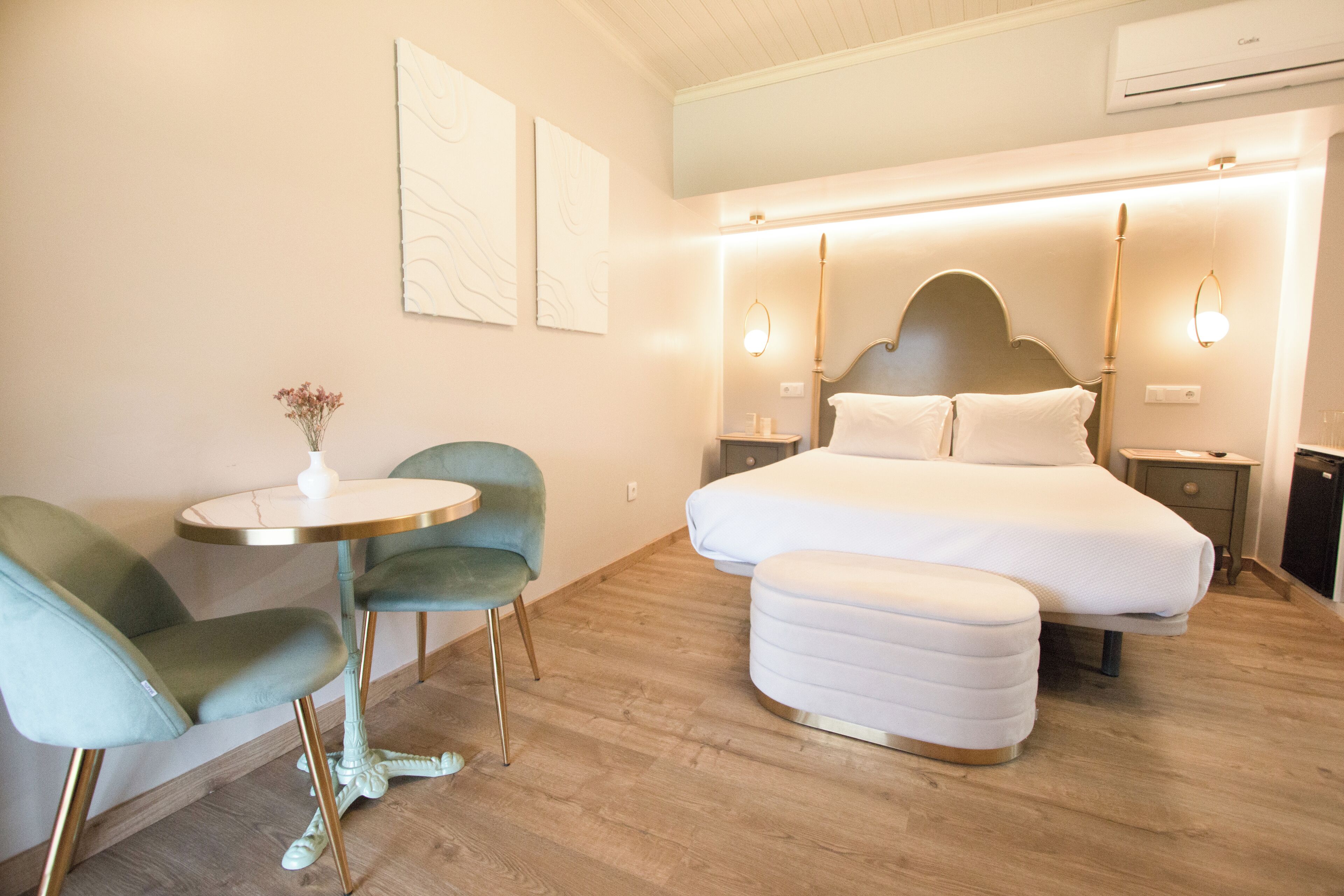 Une chambre à coucher moderne avec un grand lit, des tables de chevet, une petite table ronde avec une chaise et un vase décoratif.
