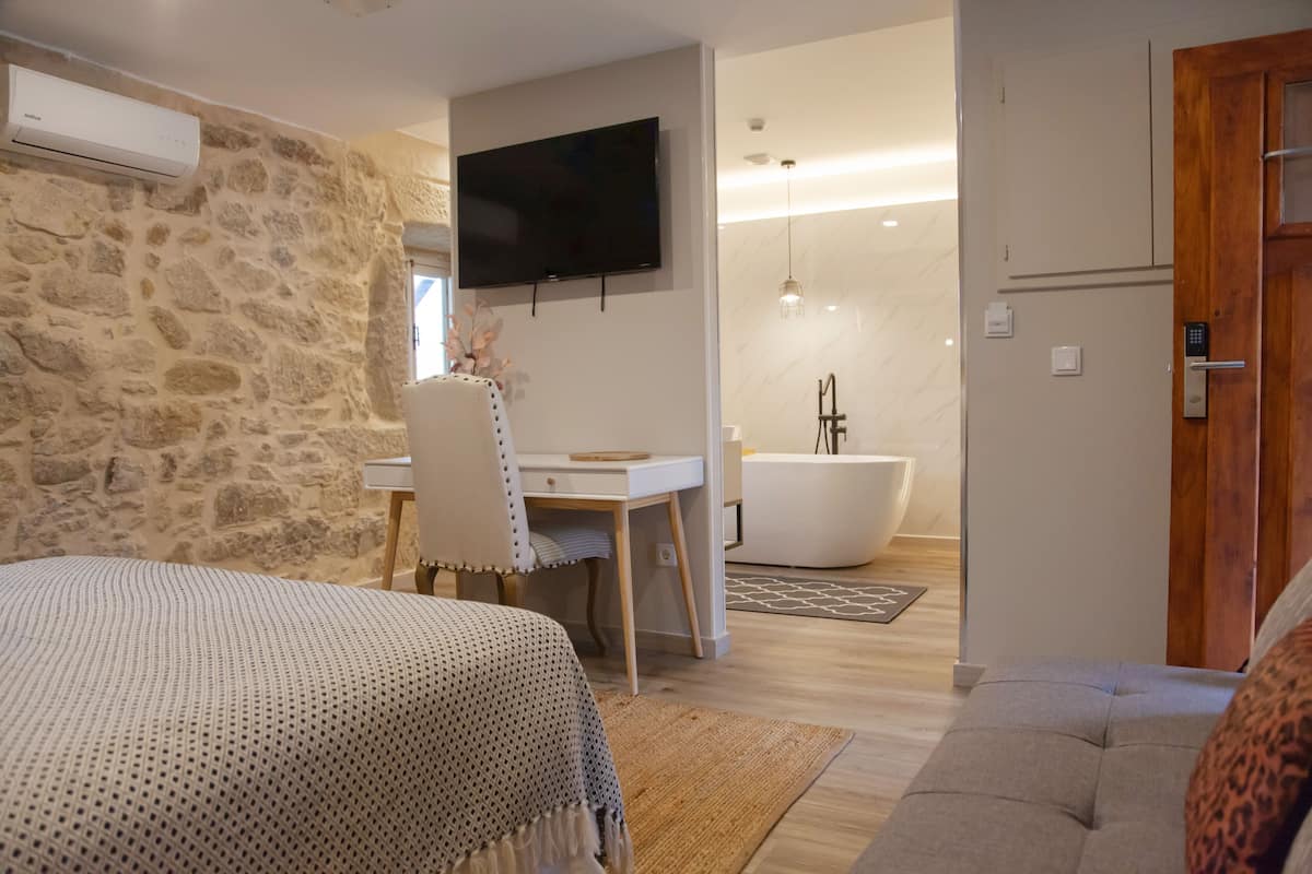 A bedroom with a bed, a desk, a chair, a TV, and a bathroom with a bathtub and shower.