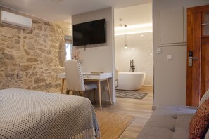 A bedroom with a bed, a desk, a chair, a TV, and a bathroom with a bathtub and shower.