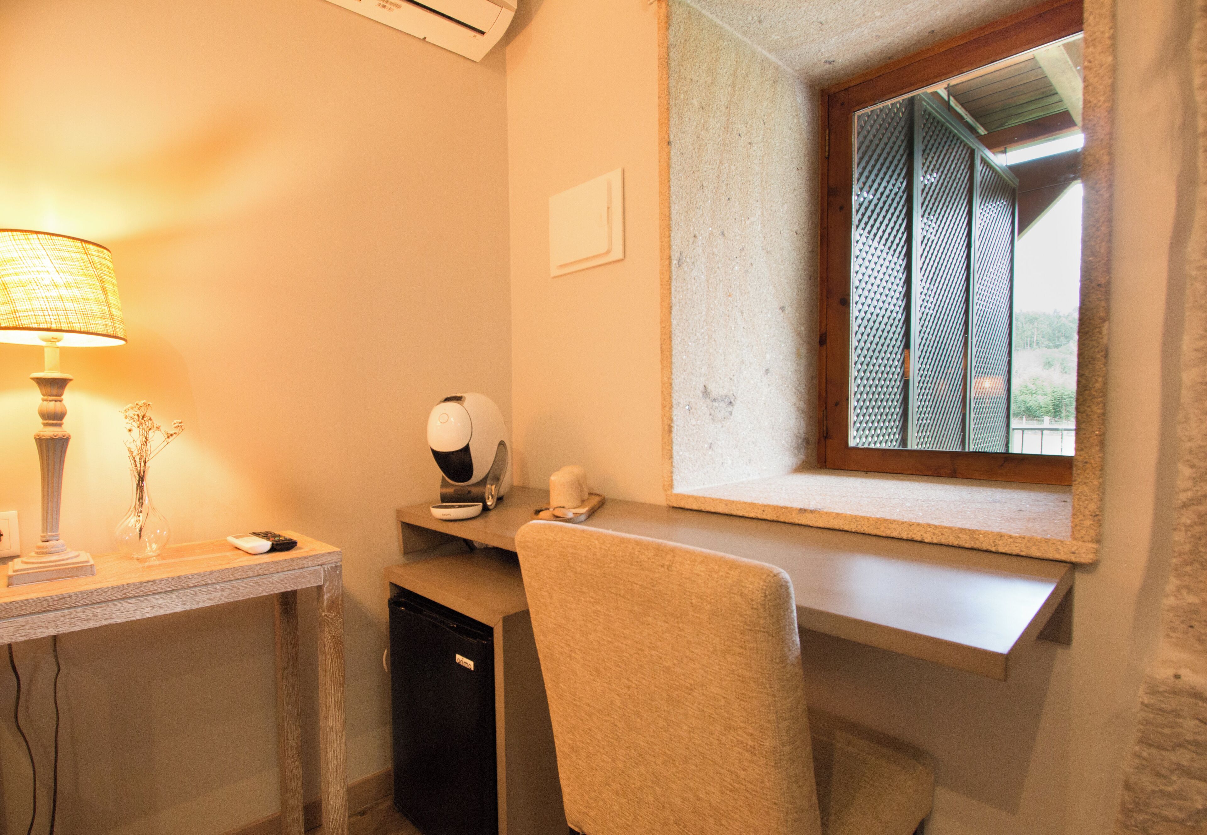 A small office with a desk, chair, lamp, and window with a view of greenery.