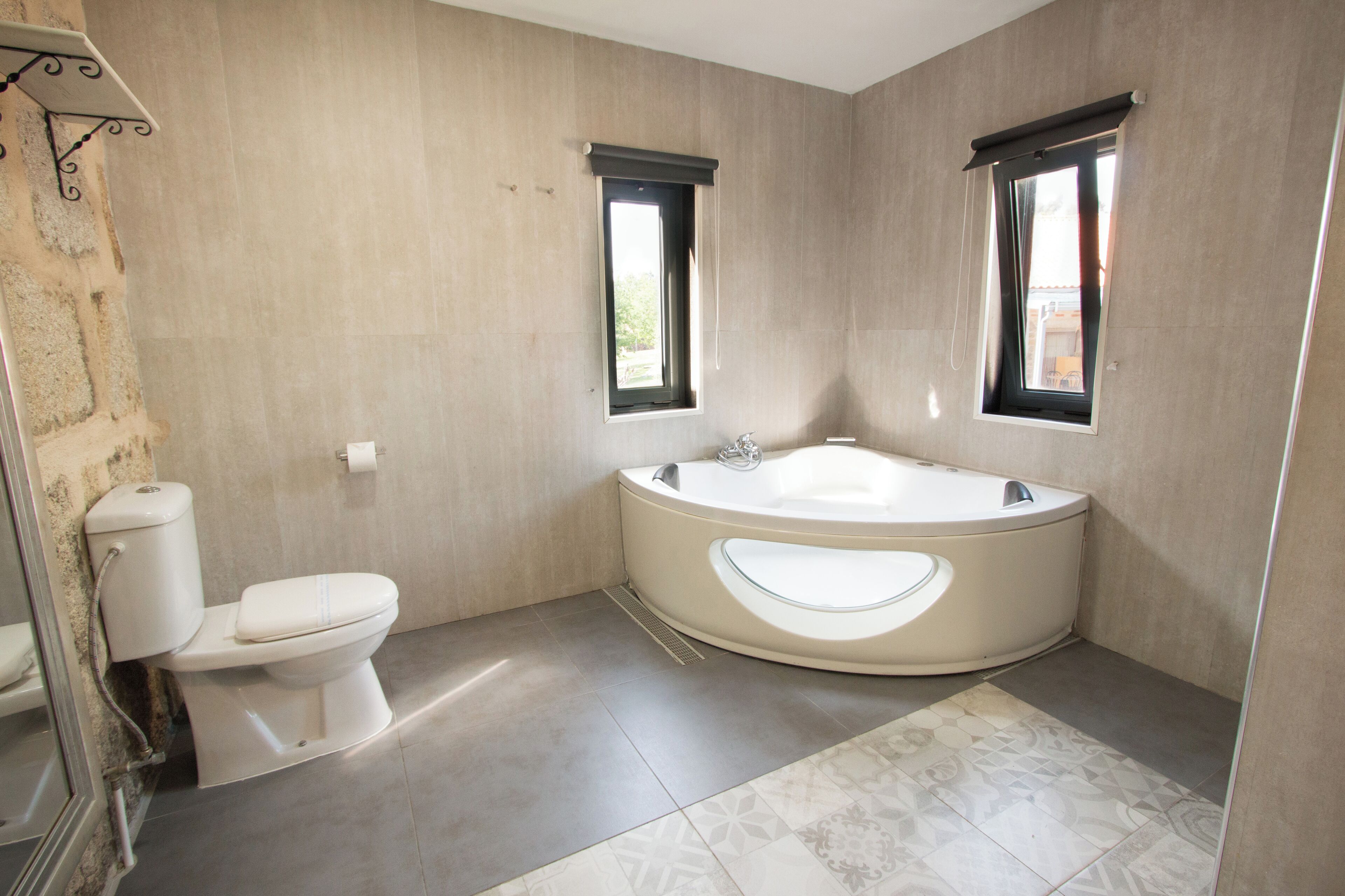 A modern bathroom with a toilet, bathtub, and two windows.
