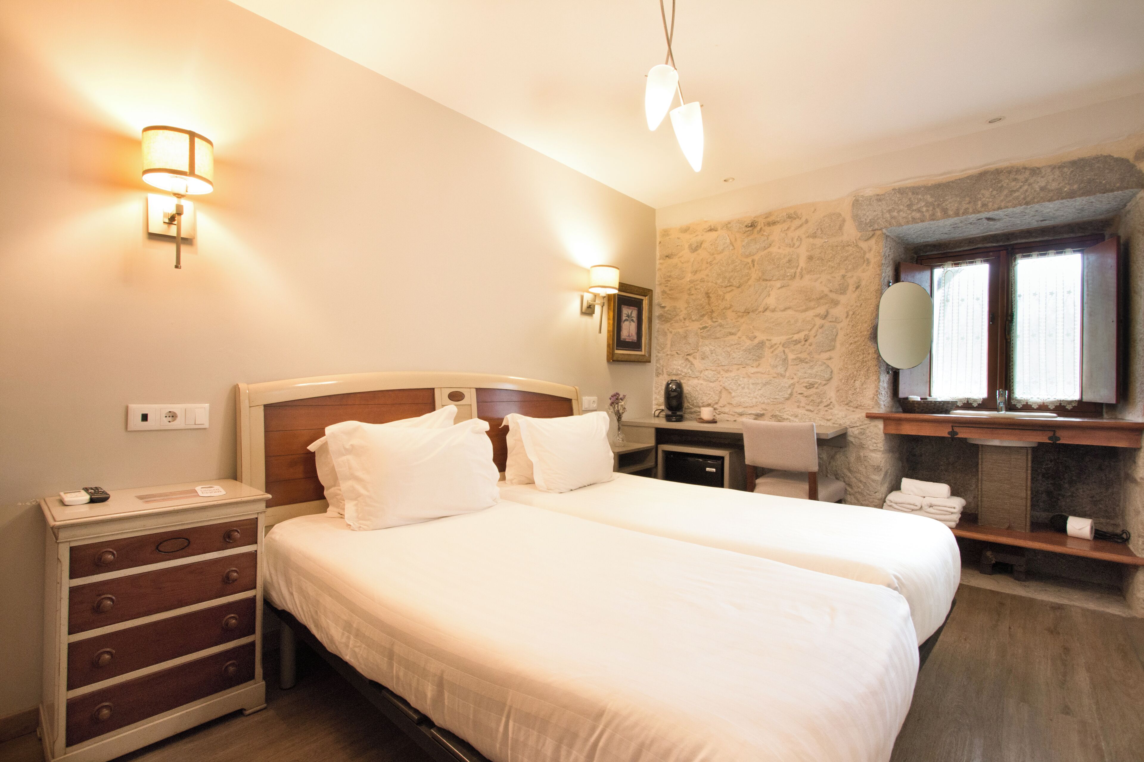 Habitación de hotel con dos camas, tocador, cómoda y una pared de acento de piedra.