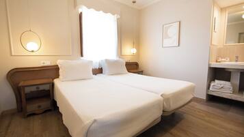 A hotel room with two beds, a nightstand, a mirror, and a bathroom with a sink and towel rack.