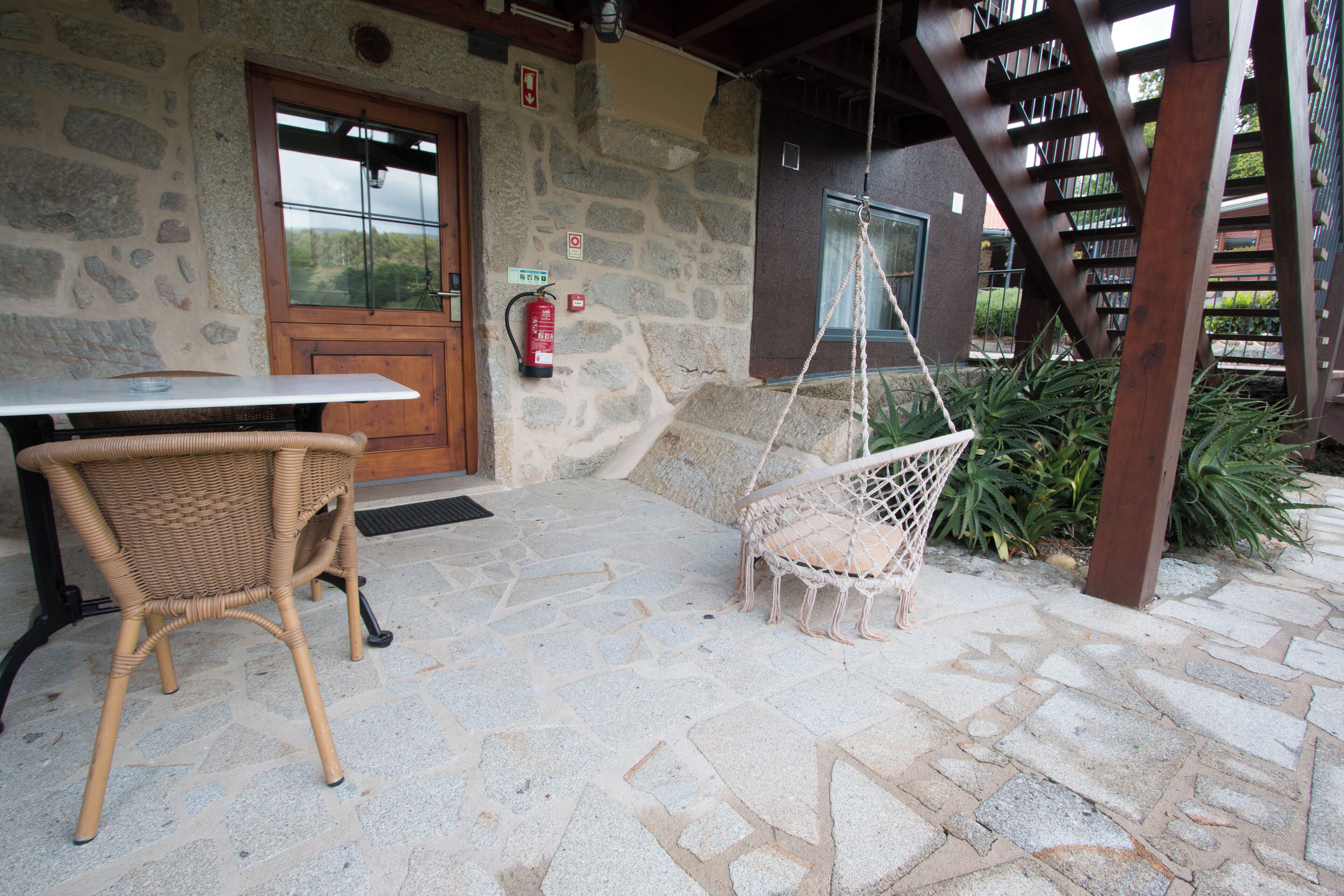 Un patio de piedra con una mesa y sillas de mimbre, una silla colgante y una escalera de madera.