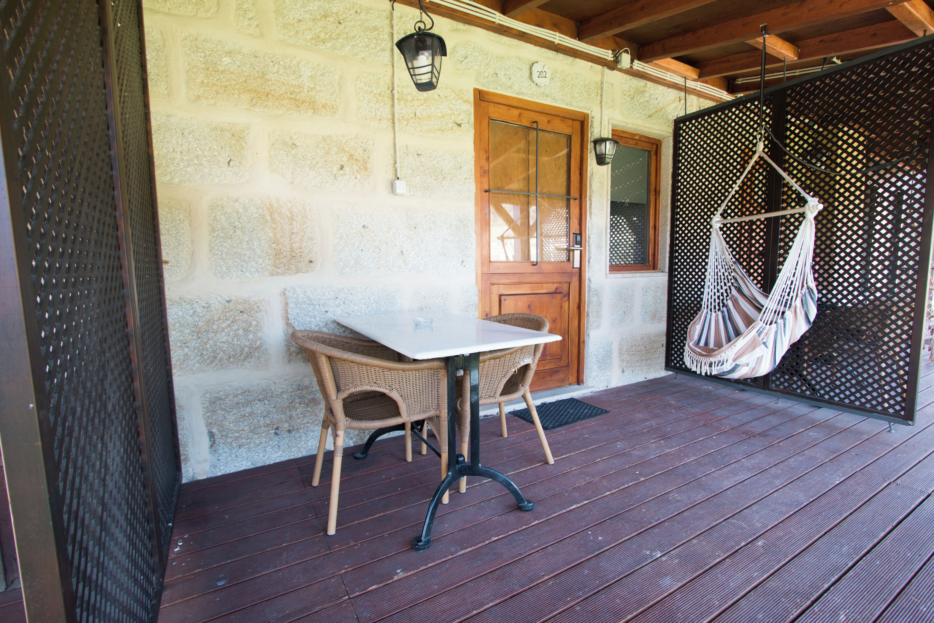 Una terraza de madera con una mesa y sillas, una hamaca colgante y una puerta de madera.
