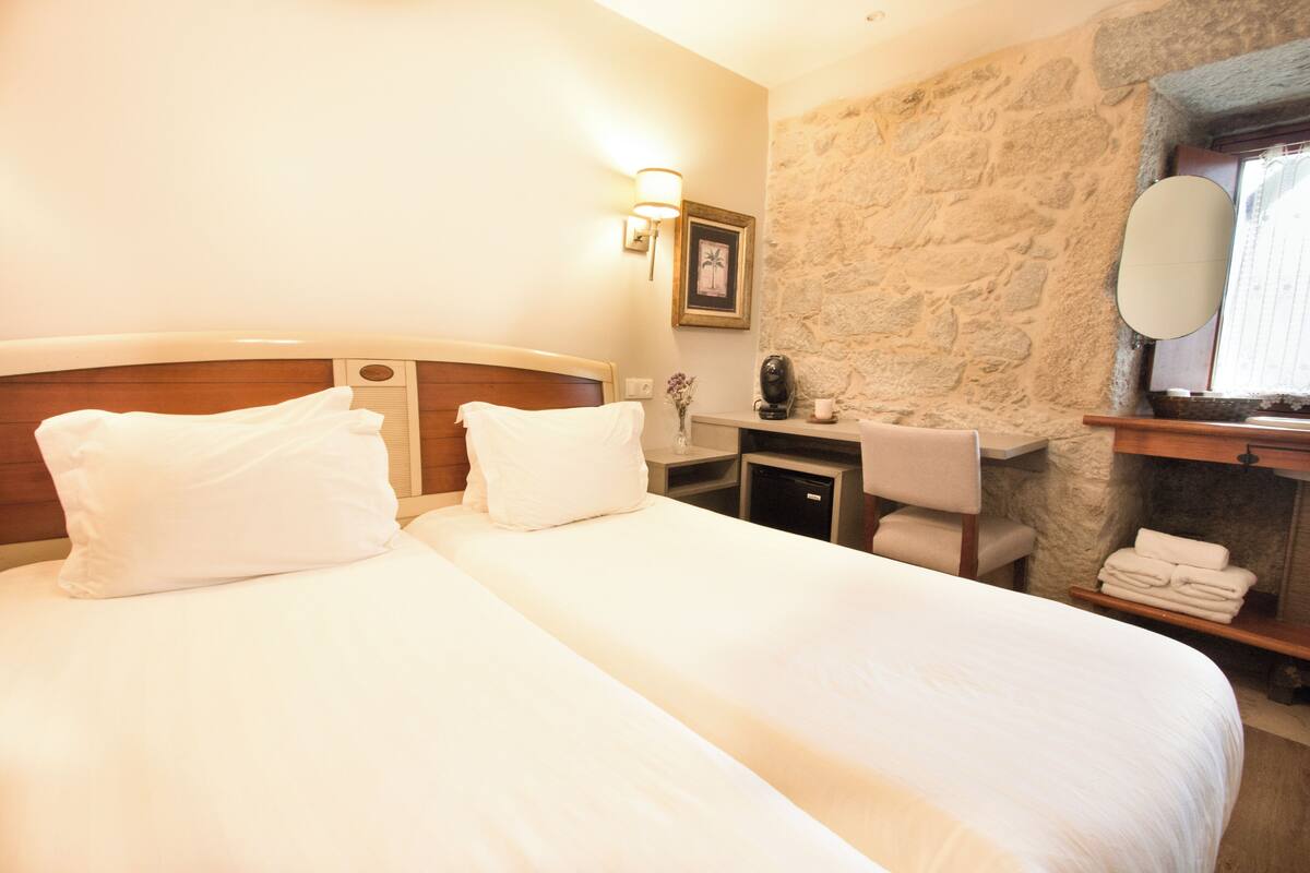 A hotel room with a large bed, a bedside table, a mirror, and a stone wall.
