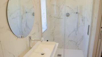 A bathroom with a marble sink, a mirror, and a glass-enclosed shower.