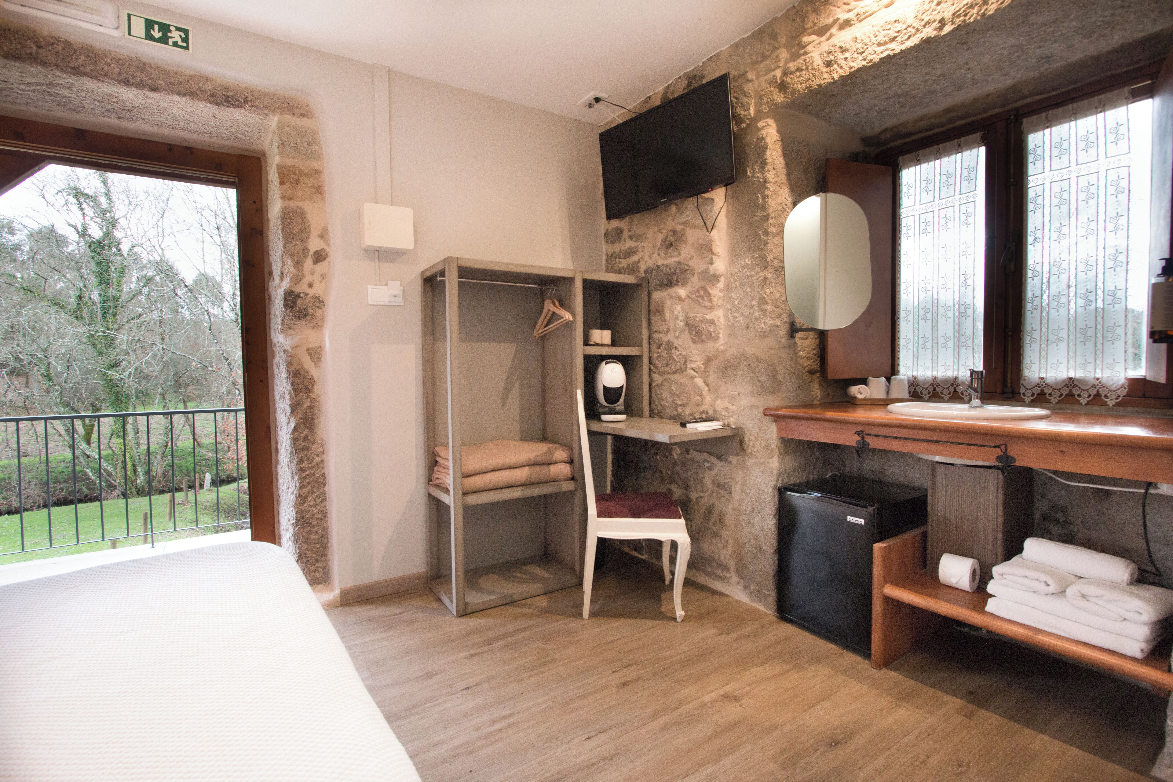 A hotel room with a bed, a wardrobe, a small desk with a chair, a mirror, and a bathroom with a sink and toilet.