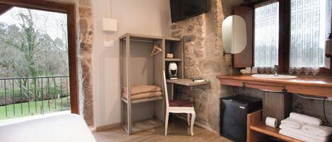 Una habitación de hotel con cama, armario, escritorio pequeño con silla, espejo y baño con lavabo e inodoro.