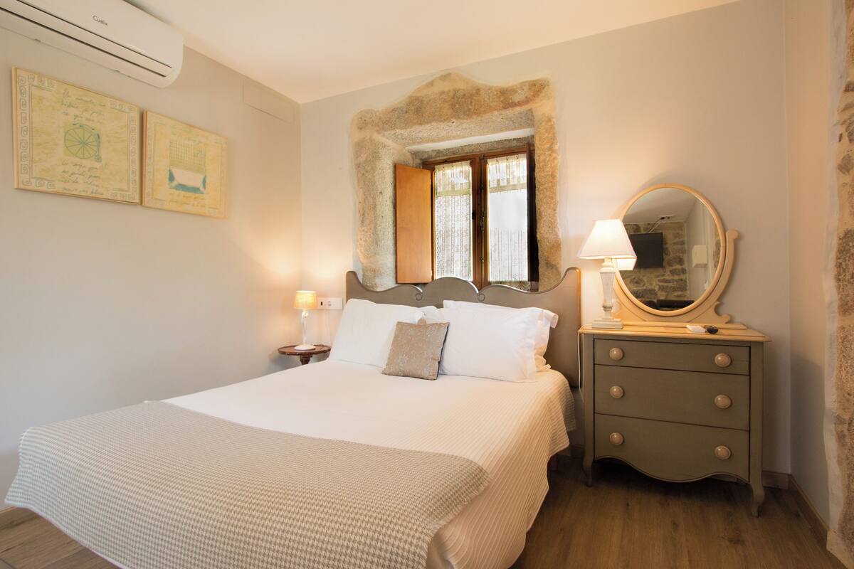 A bedroom with a bed, a dresser, a mirror, and two wall-mounted air conditioning units.