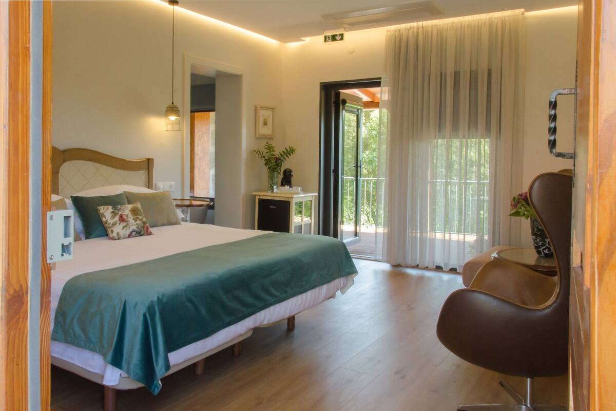A hotel room with a bed, a chair, a small table, and a view of the outdoors.