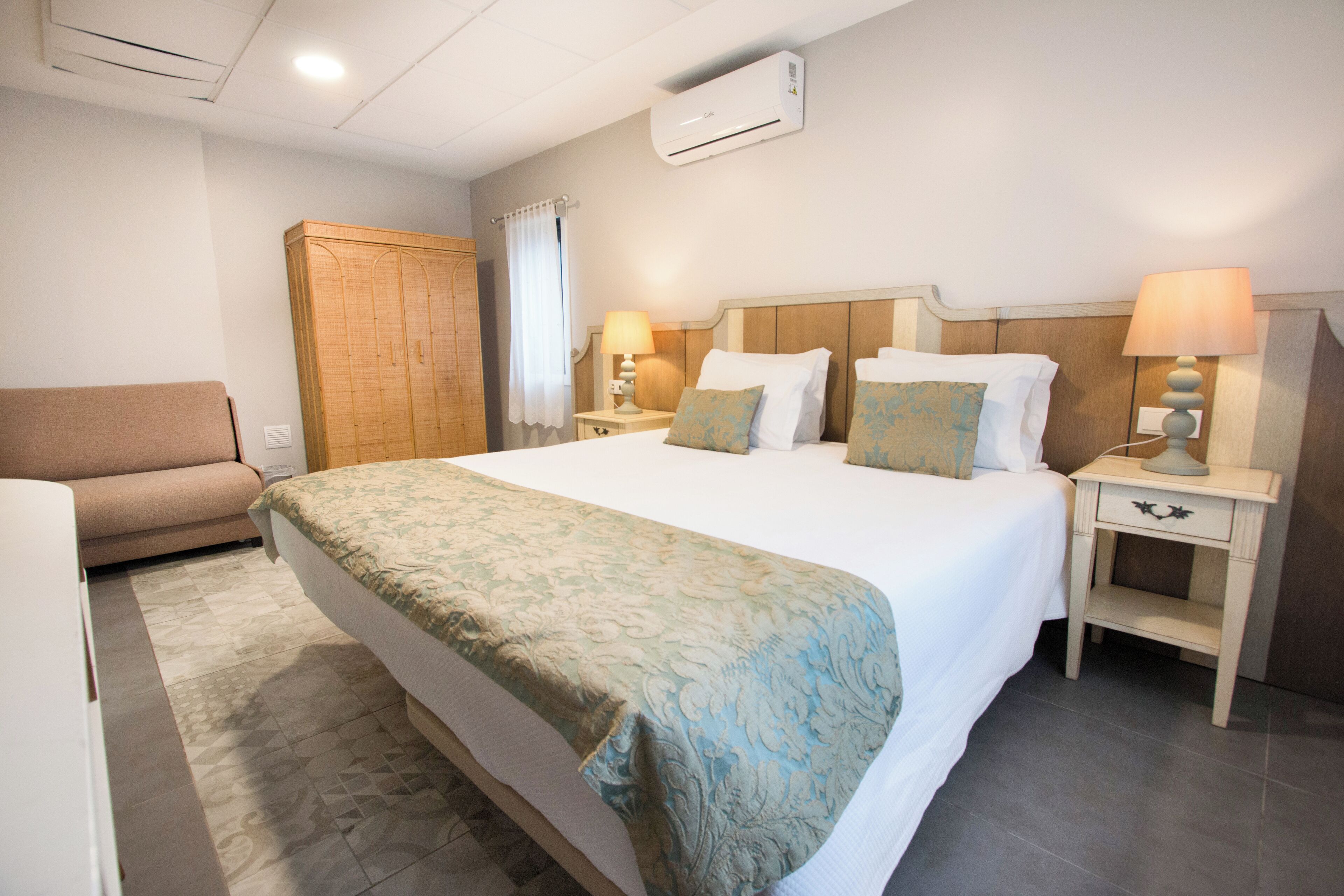 Een hotelkamer met een groot bed, nachtkastjes met lampen, een kledingkast en een bank.