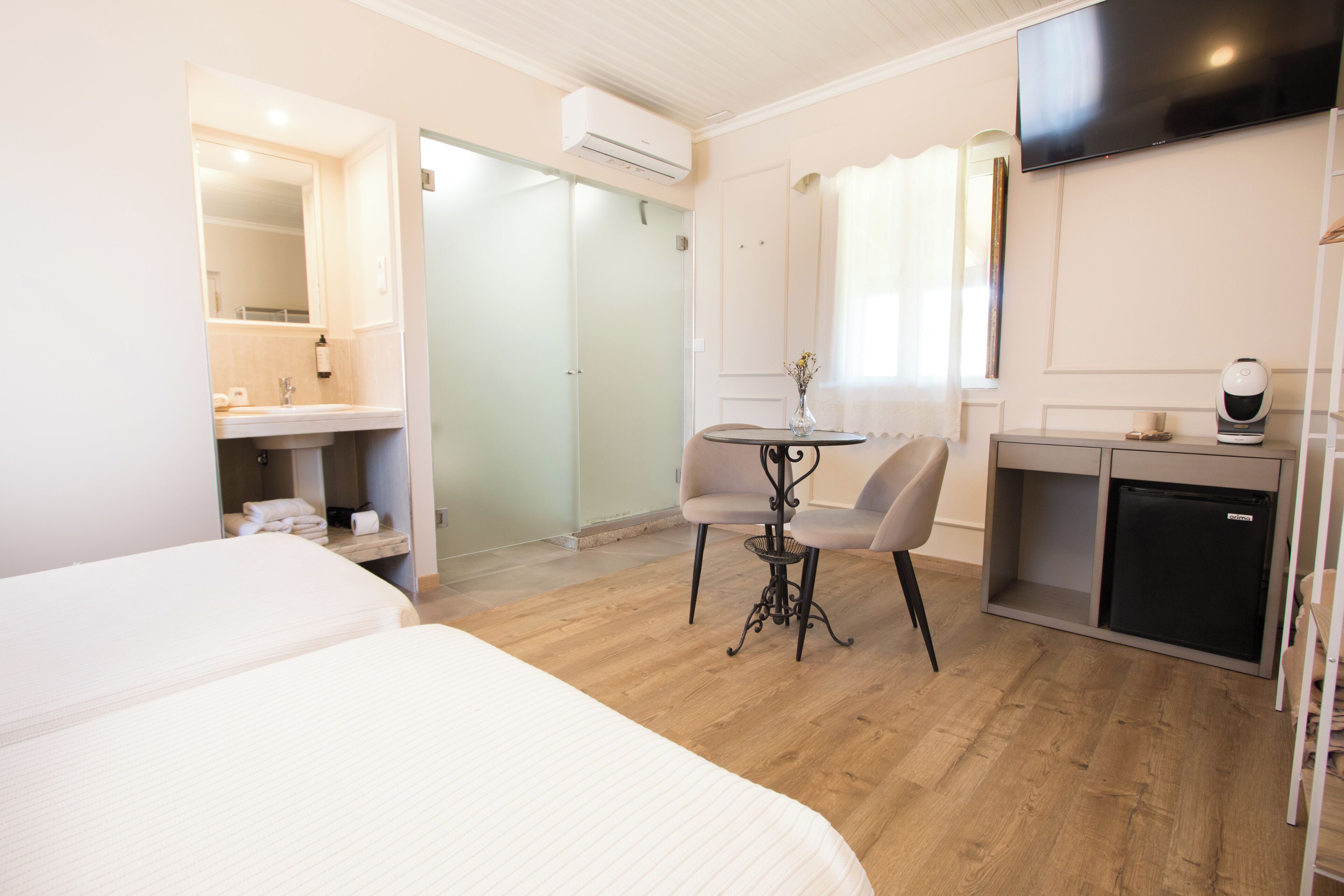 Habitación de hotel con cama, escritorio con silla, refrigerador pequeño, televisor montado en la pared y aire acondicionado.