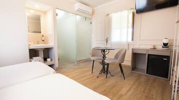Habitación de hotel con cama, escritorio con silla, refrigerador pequeño, televisor montado en la pared y aire acondicionado.