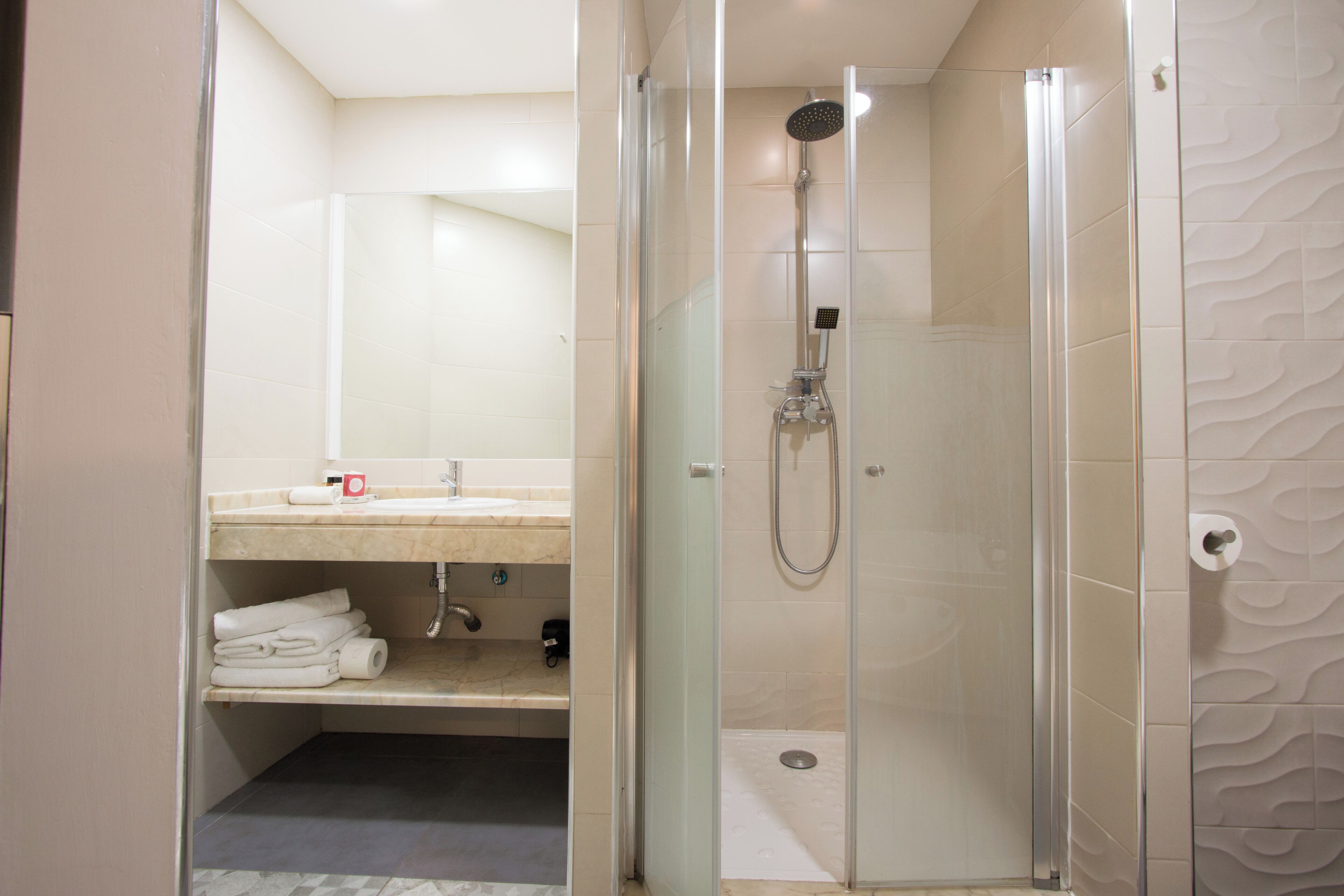 Une salle de bain moderne avec une douche à parois de verre, un meuble-lavabo avec un miroir et des serviettes soigneusement pliées sur une étagère.