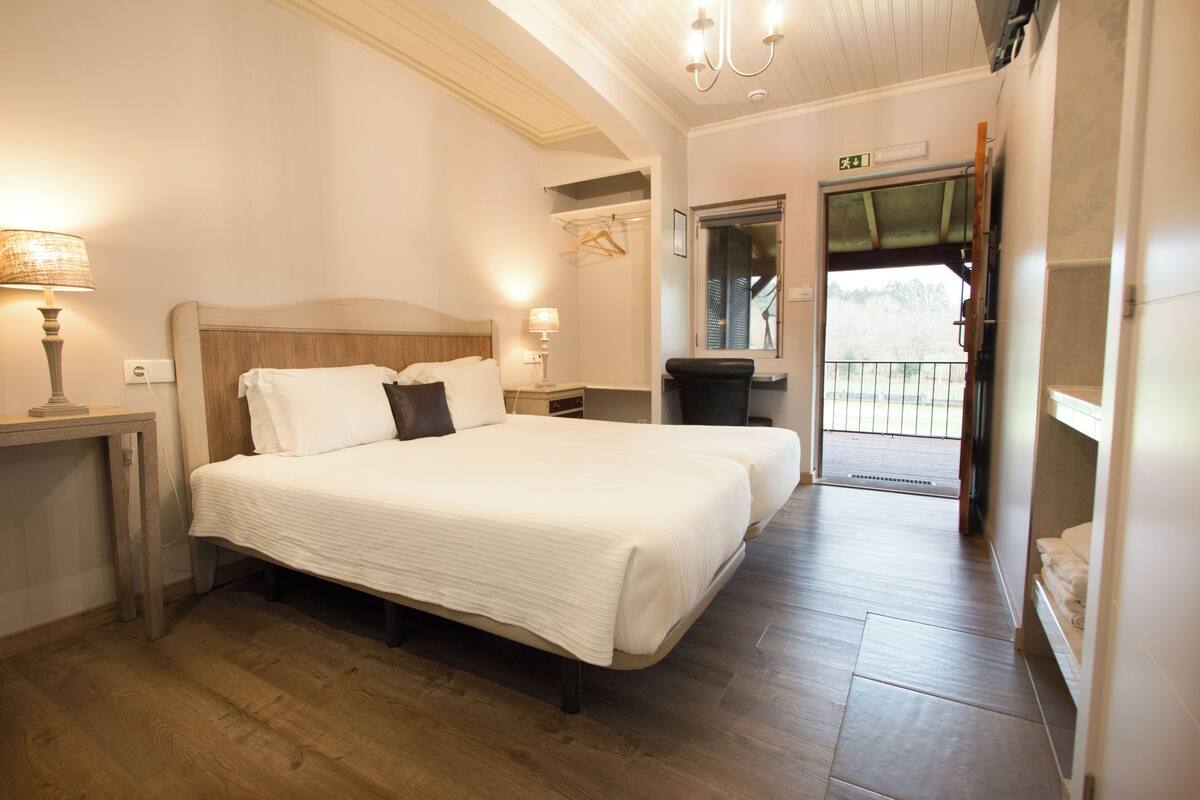 A bedroom with a large bed, bedside tables, a lamp, and a view of the outside.